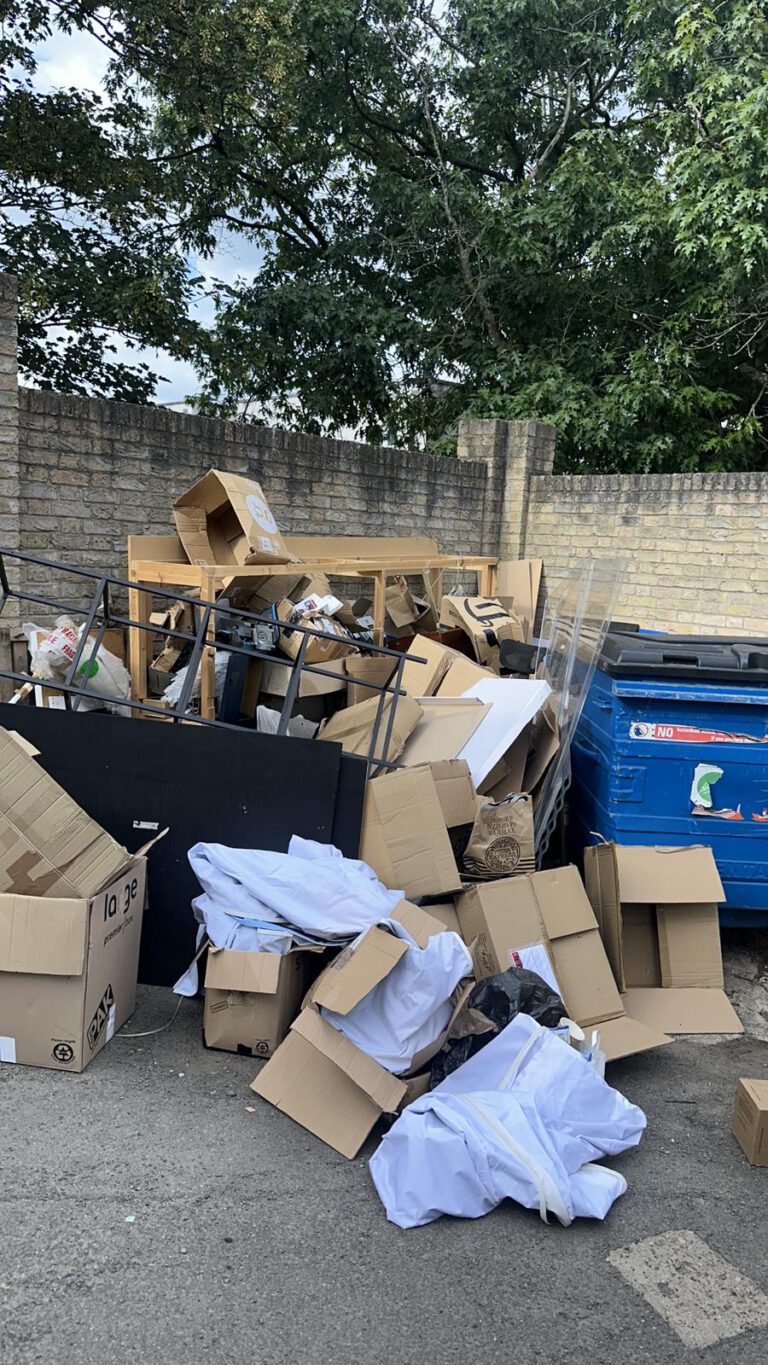 Cardboard and waste piled beside commercial bins before collection